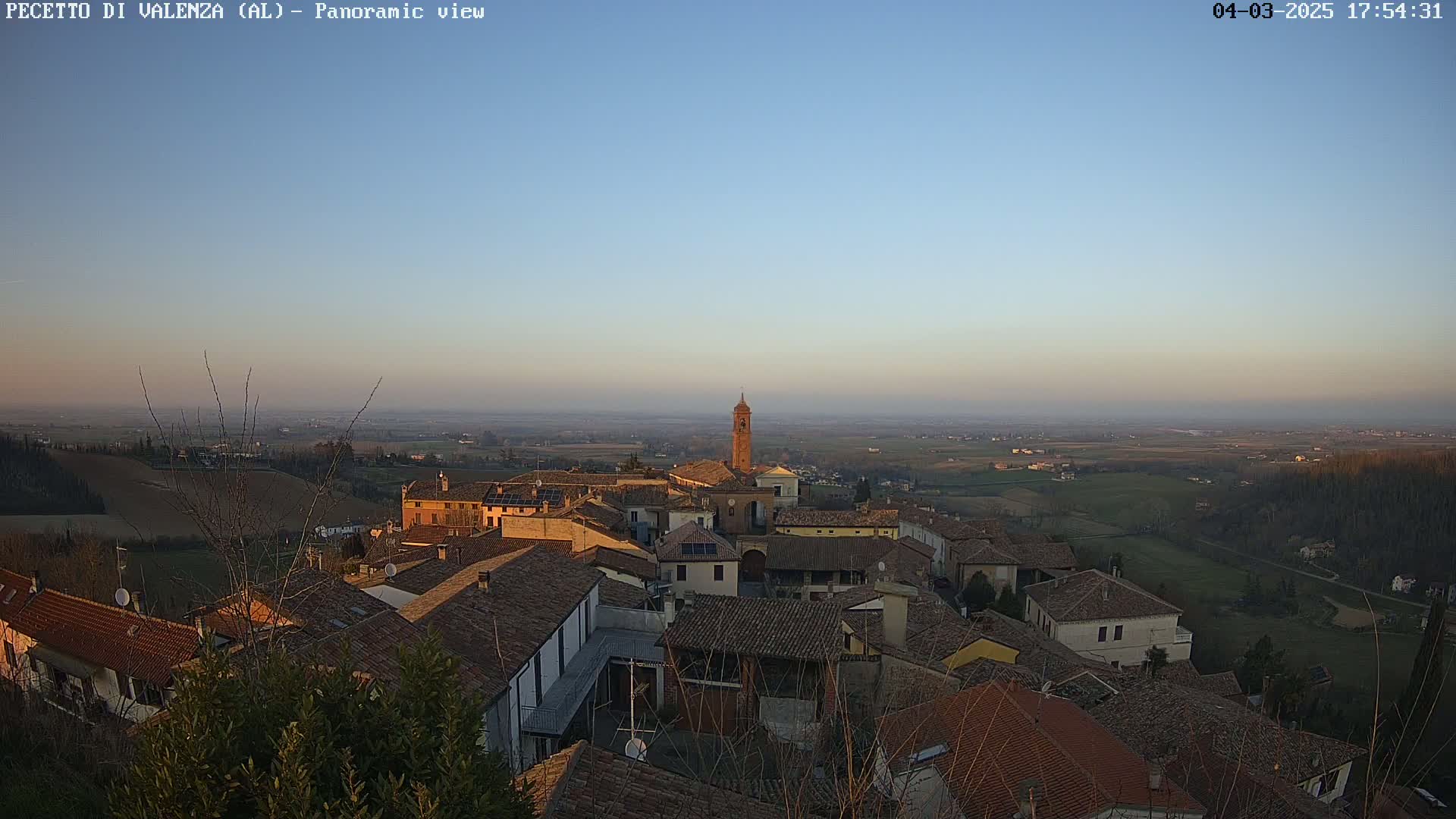 An aerial view of a small town with red-tiled roofs, nestled in a valley at sunset under a clear sky.