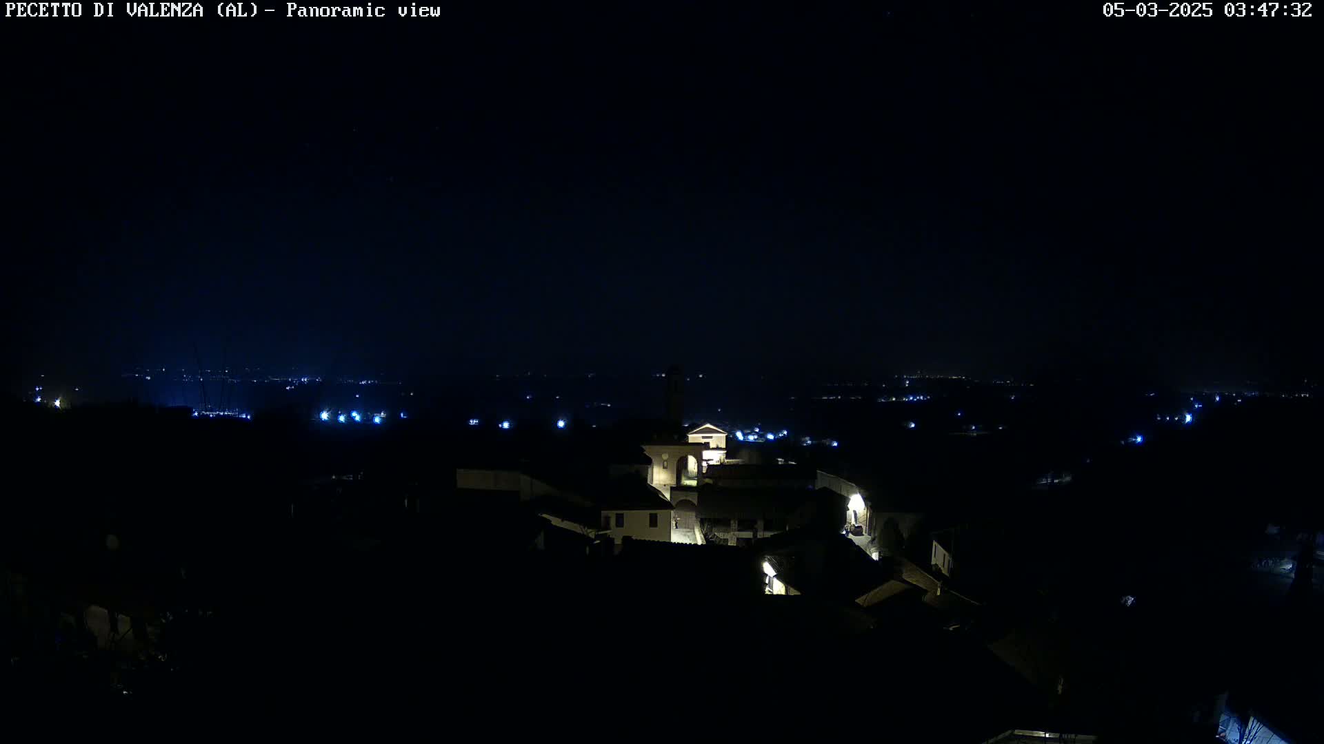 A nighttime panoramic view of a small village with dimly lit buildings, set against a dark sky.