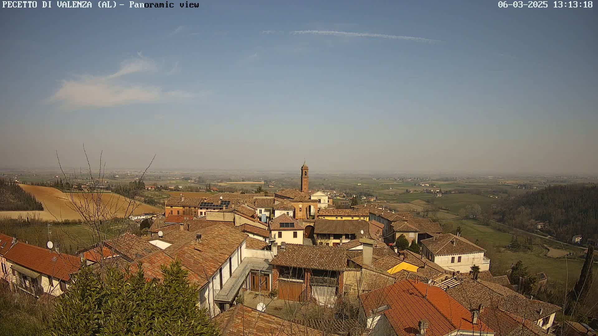 A panoramic view of a small town nestled in a valley on a sunny day with a few wispy clouds in the sky.