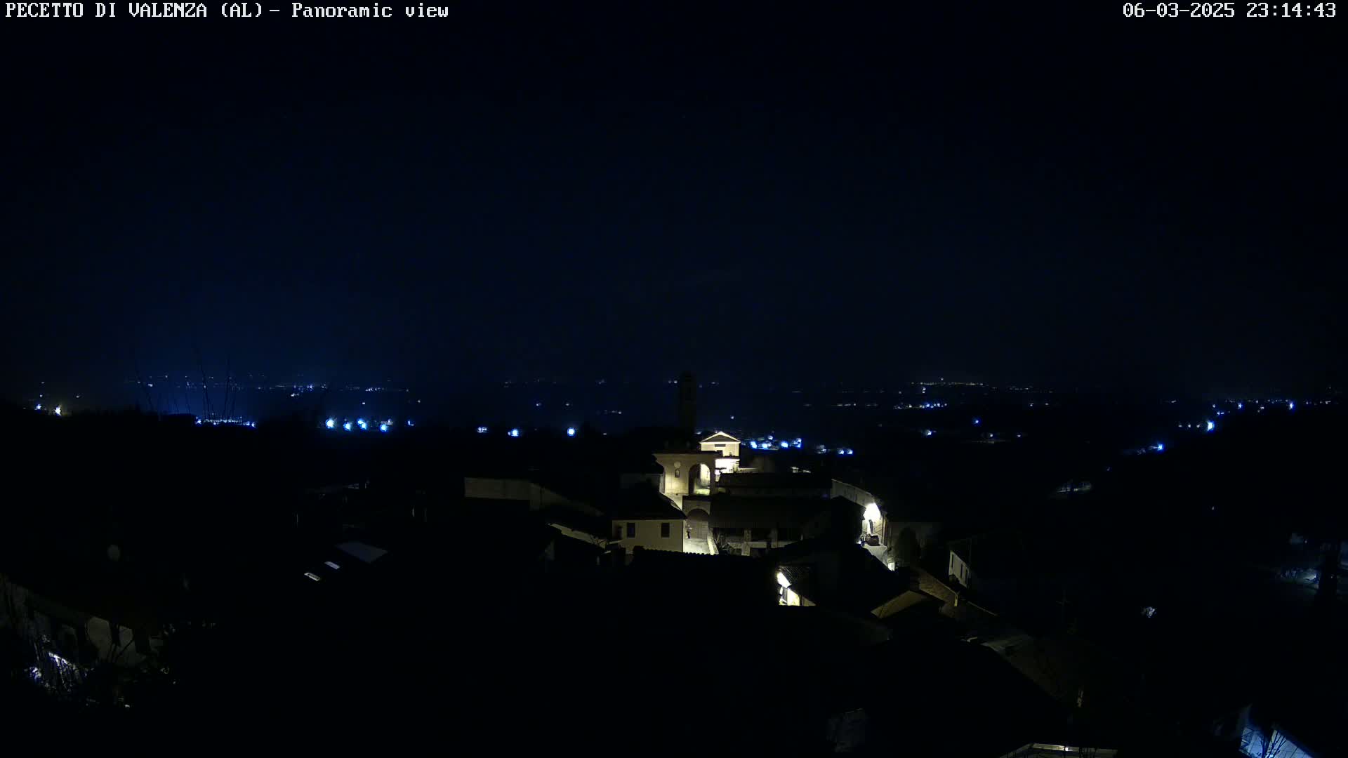 A nighttime panoramic view shows a small town illuminated with faint lights against a dark sky.