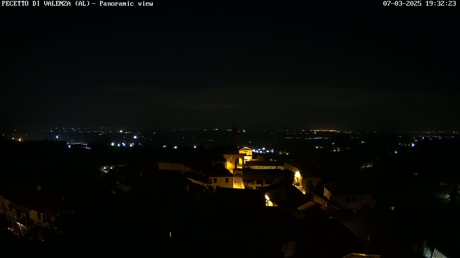 A nighttime panoramic view shows a small town illuminated by scattered lights against a dark, clear sky.