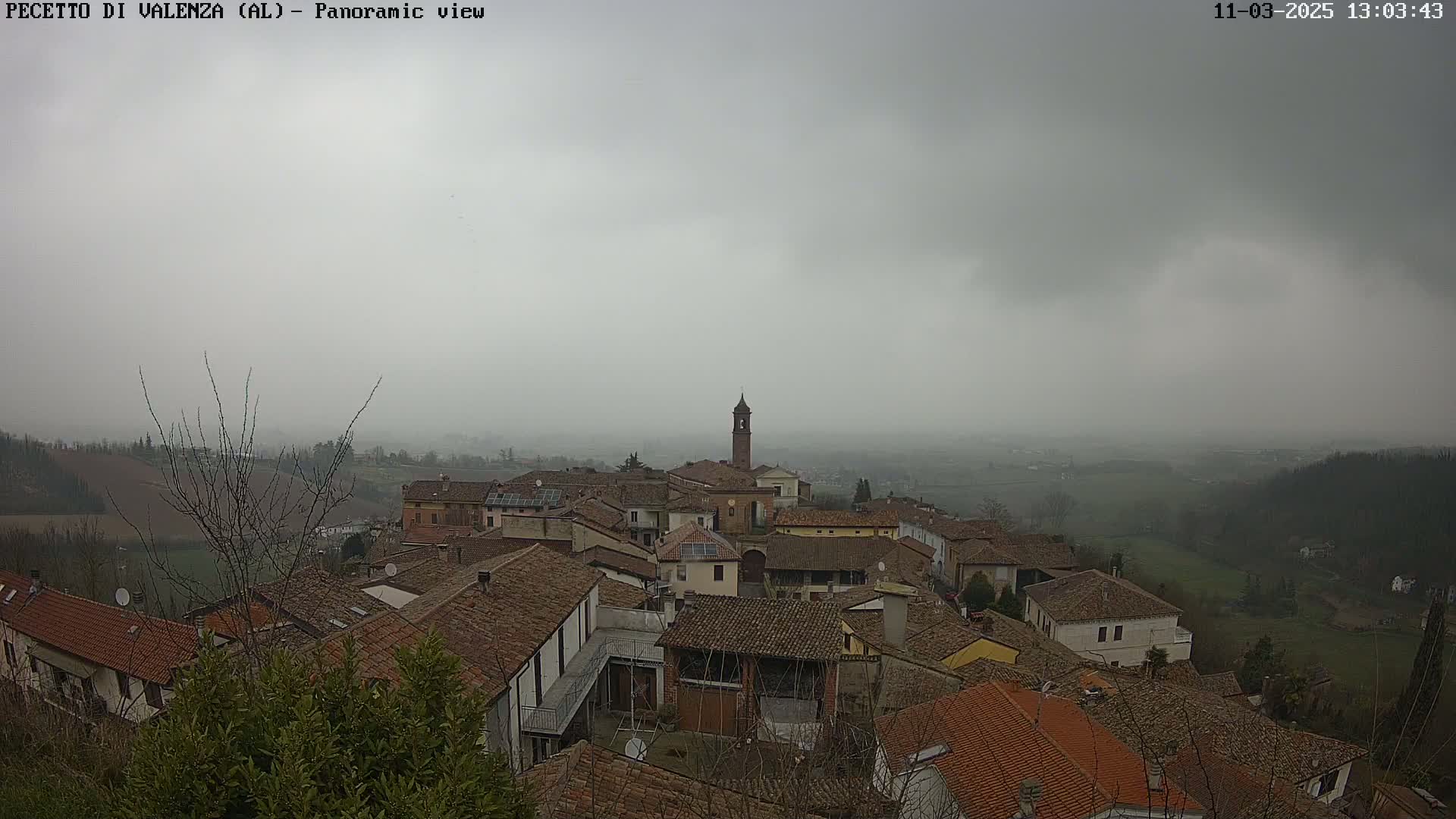 A panoramic view of a small town with red tile roofs under a hazy, overcast sky.