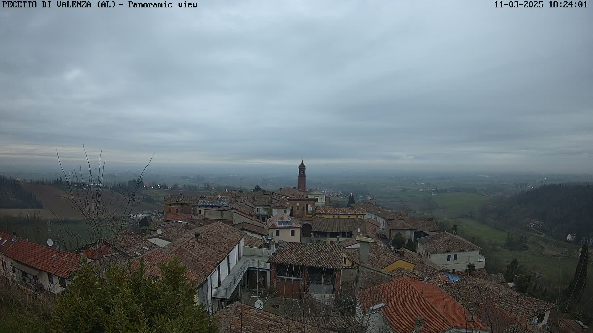 A panoramic view of a town with red-tiled roofs under a cloudy sky.