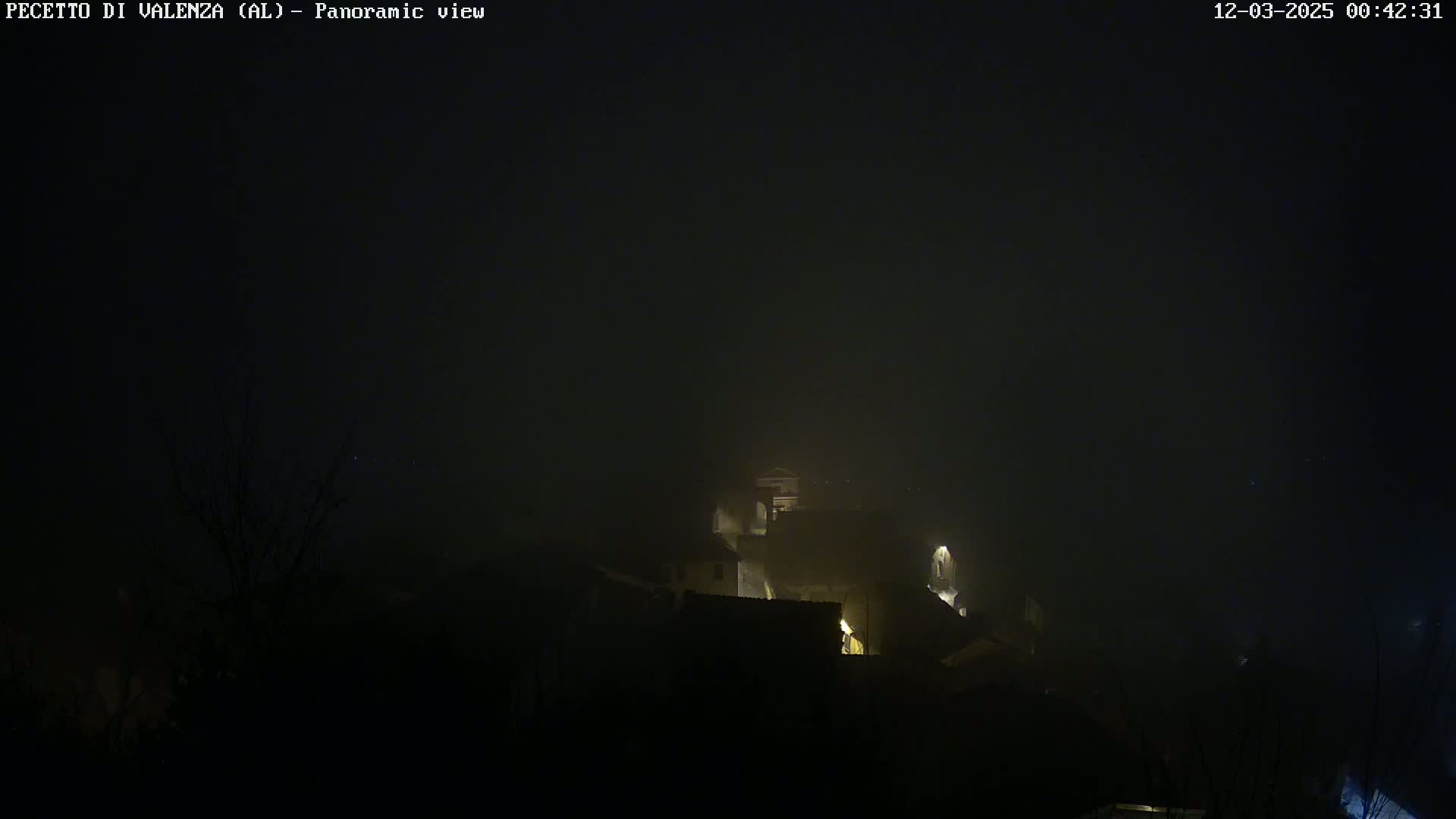 A foggy night scene shows a dimly lit village nestled in the hills.