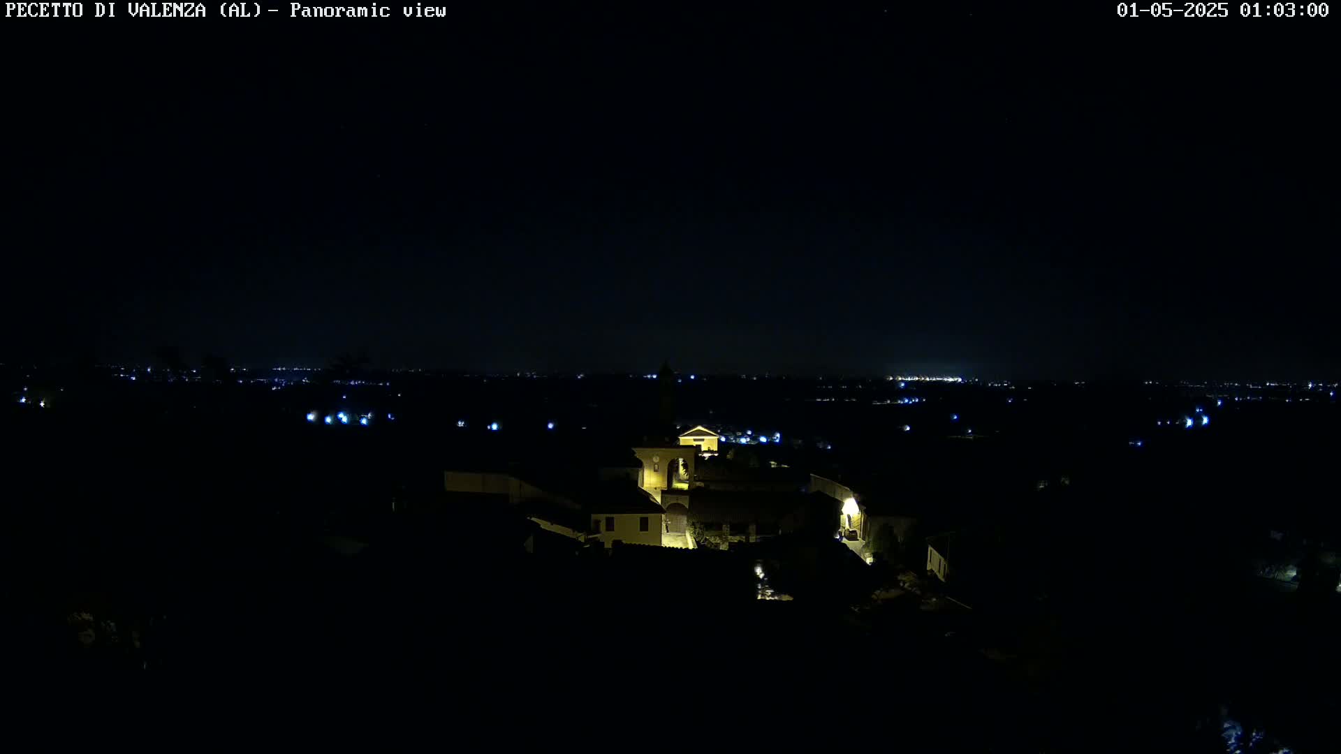 A nighttime panoramic view shows a small village illuminated with scattered lights against a dark sky.
