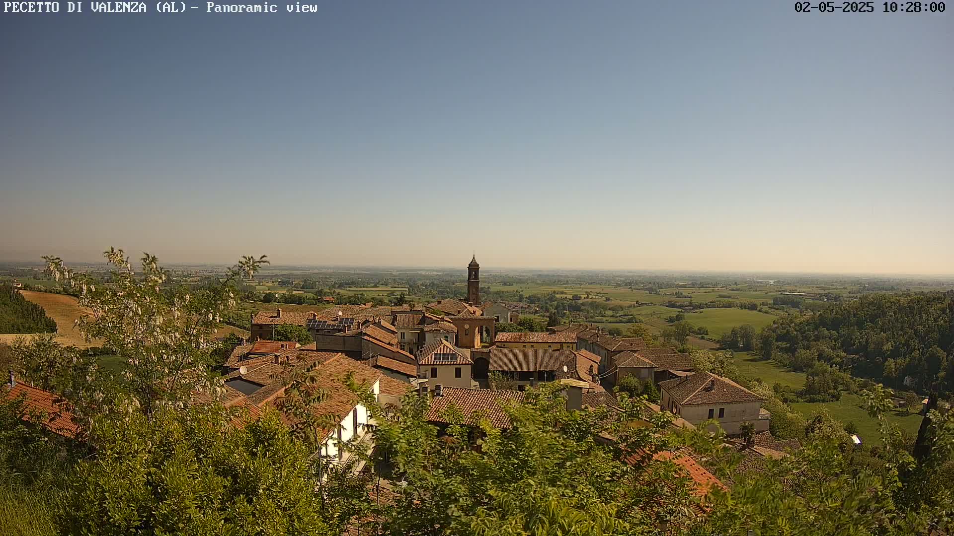 A panoramic view of a small town nestled in a verdant valley under a clear, bright sky.