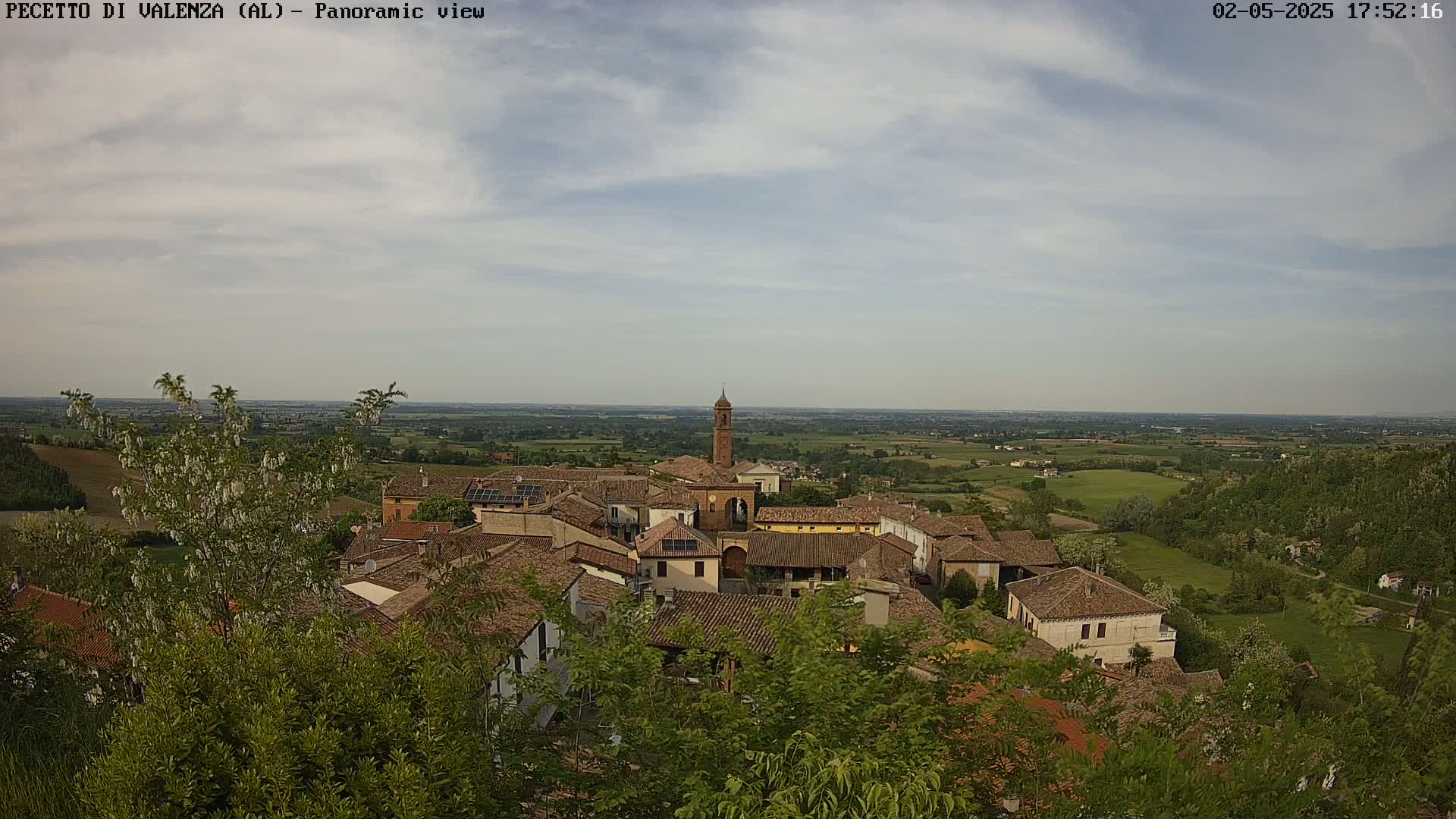 An elevated view of a small town with terracotta roofs nestled in a verdant landscape under a partly cloudy sky.