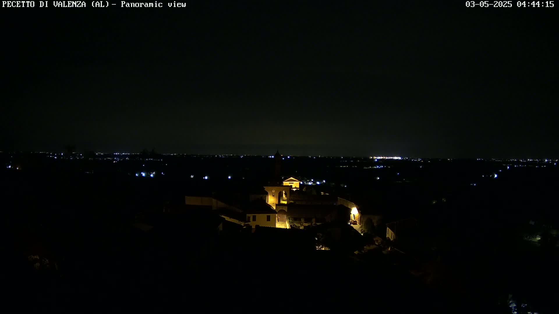 A nighttime, panoramic view shows a small village with illuminated buildings, and a distant horizon dotted with faint lights.