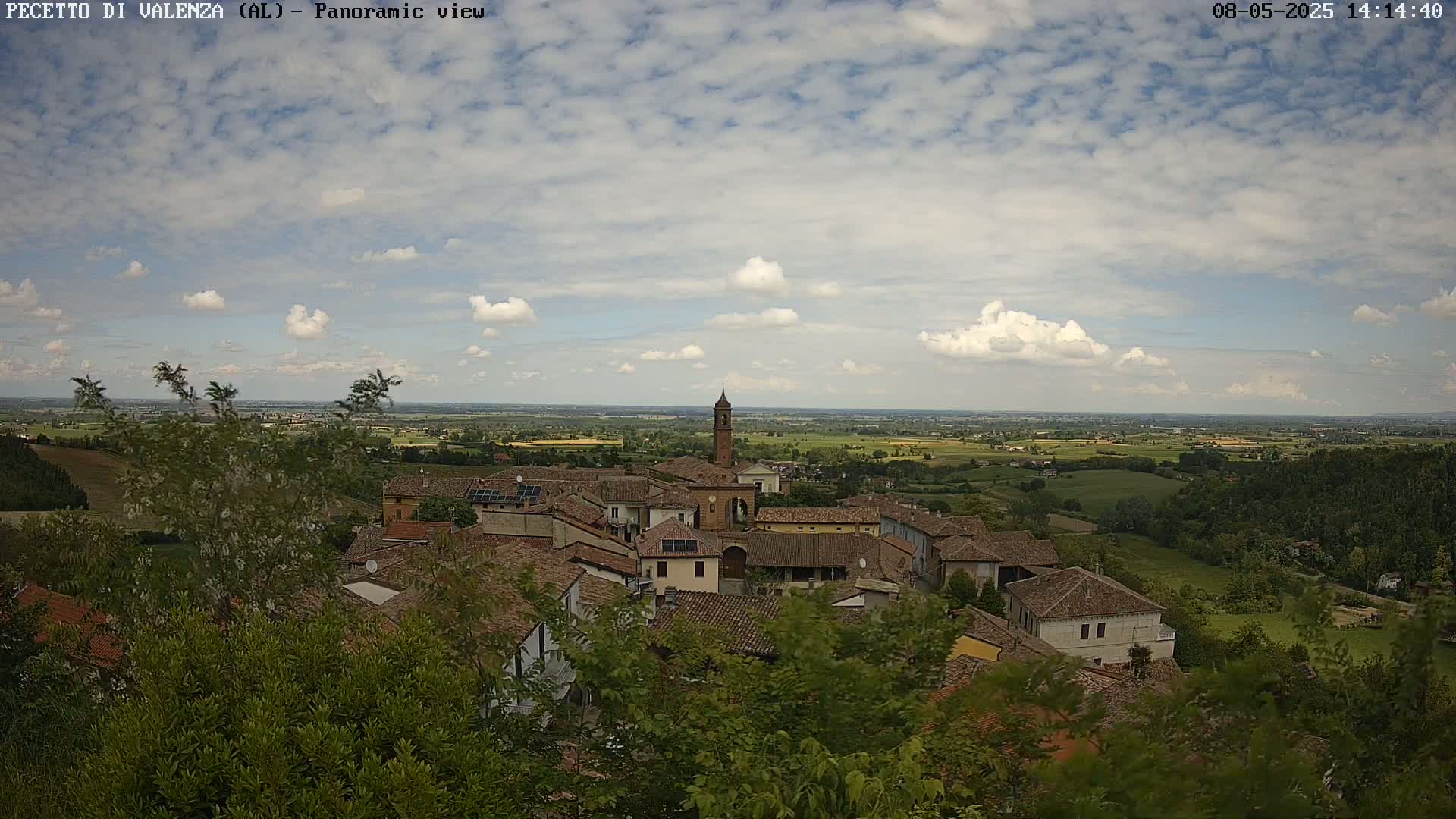 A panoramic view of a small town nestled in a verdant landscape under a partly cloudy sky.