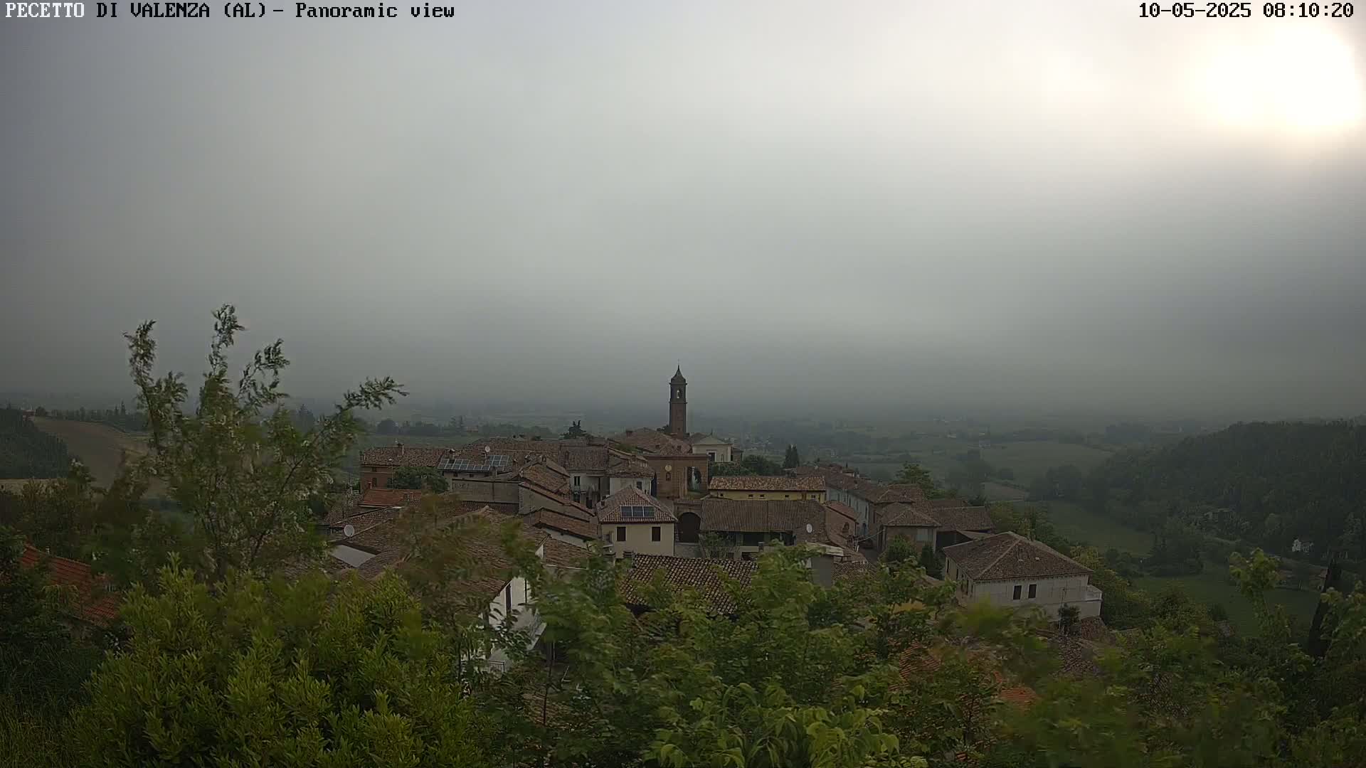 A hazy, overcast view shows a small village nestled among green trees and hills.