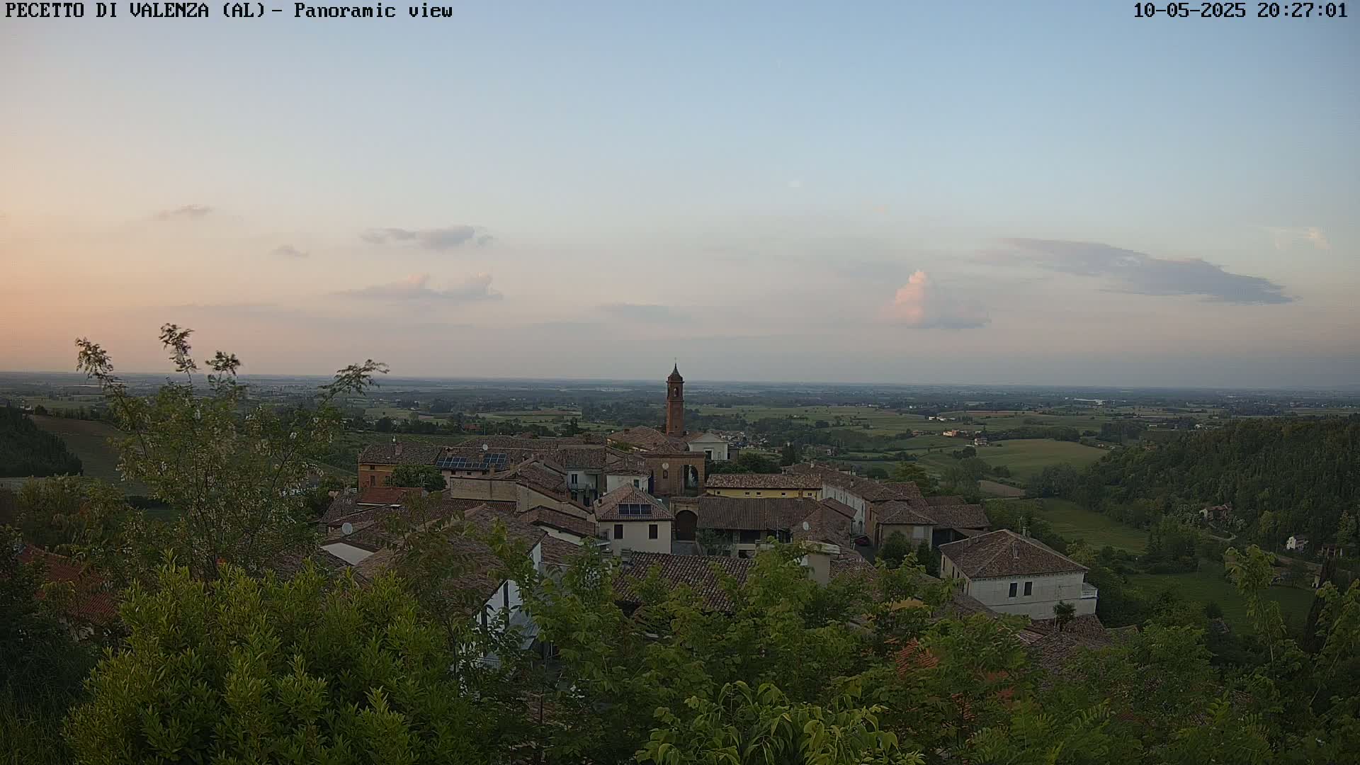 A panoramic view of a small town nestled in a verdant valley at dusk, under a mostly clear sky with a few clouds.