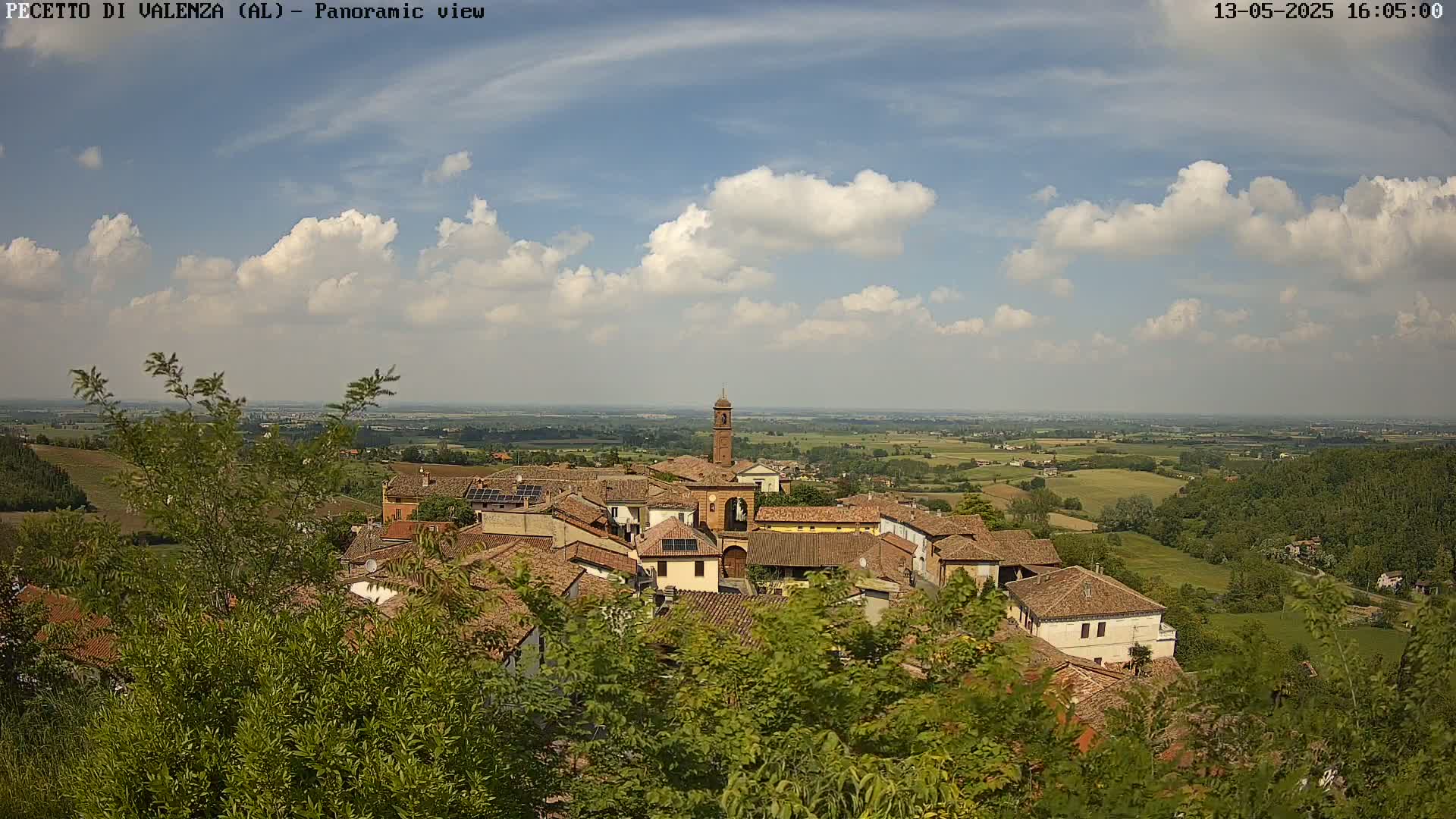 A small village with red-tiled roofs nestled in a verdant landscape under a partly cloudy sky.