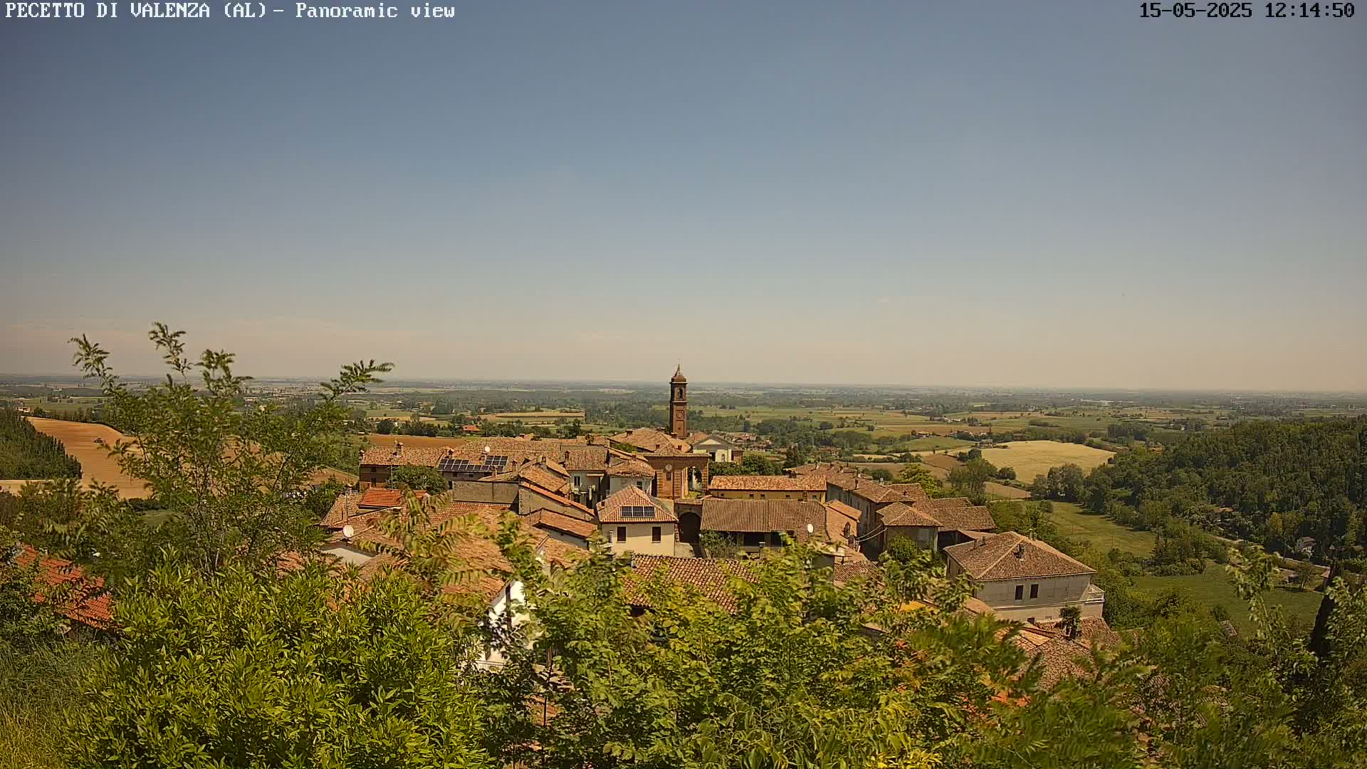A panoramic view of a small town nestled in a verdant landscape under a clear, sunny sky.