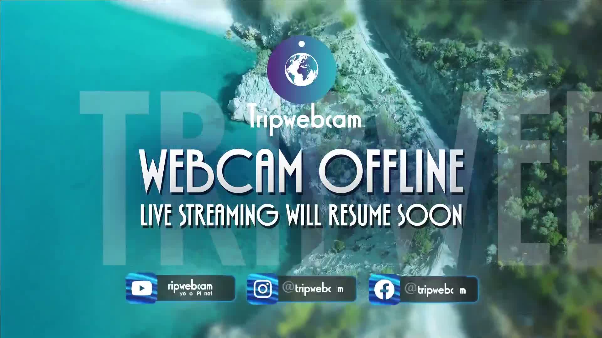 An aerial view of a rocky coastline meeting turquoise water, overlaid with a message indicating a webcam is temporarily offline.
