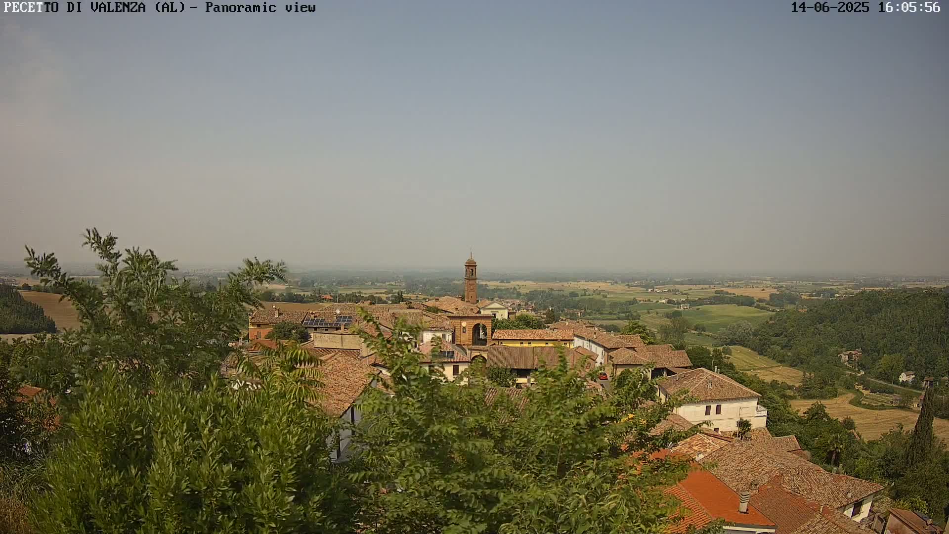 A hazy, sunny day overlooks a small village of terracotta-roofed buildings nestled in a verdant valley.