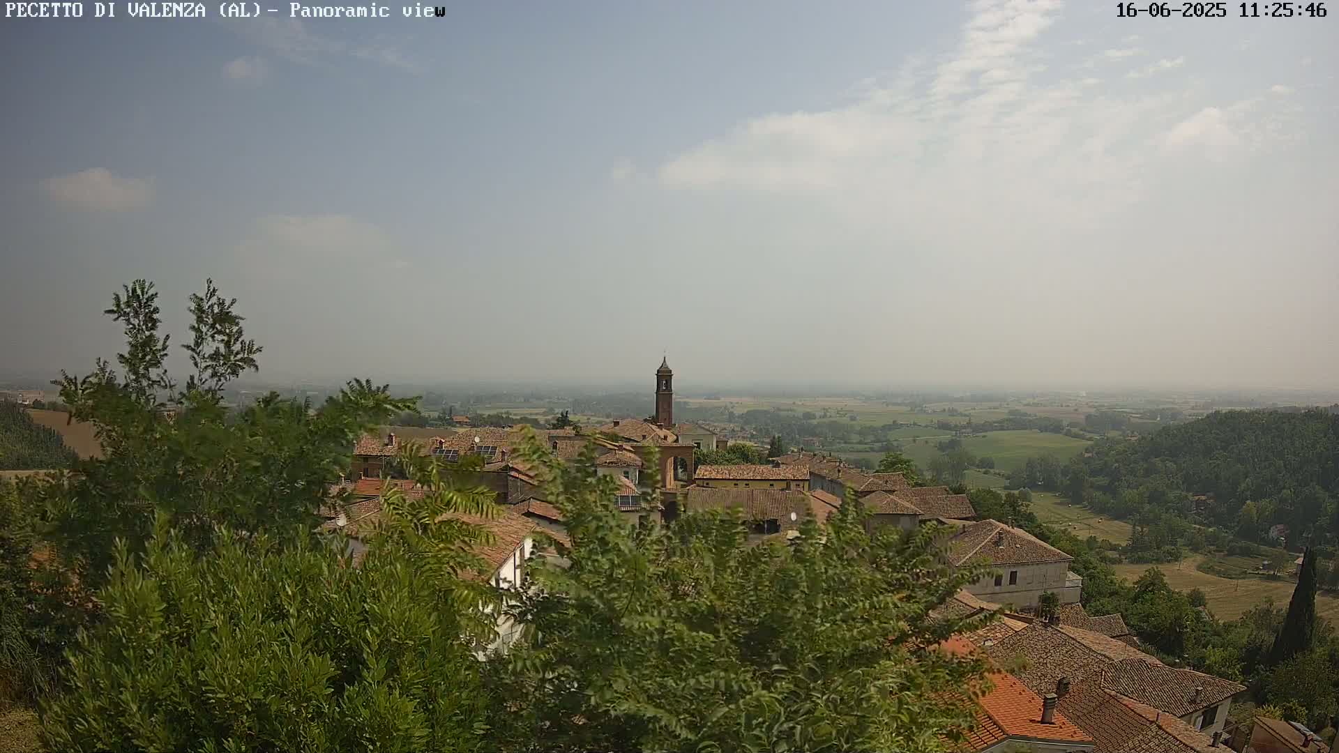 A hazy, sunny day overlooks a quaint village nestled among lush green vegetation and rolling hills.