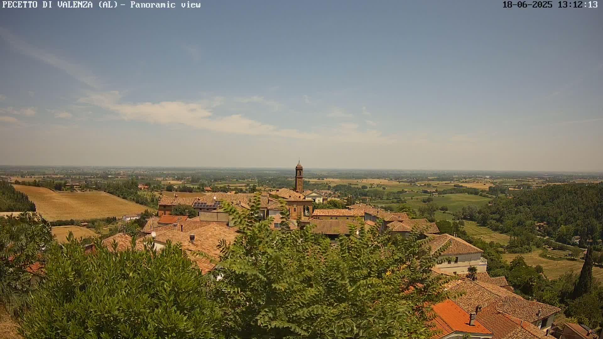 A panoramic view shows a town nestled in a hilly landscape under a mostly clear, sunny sky.