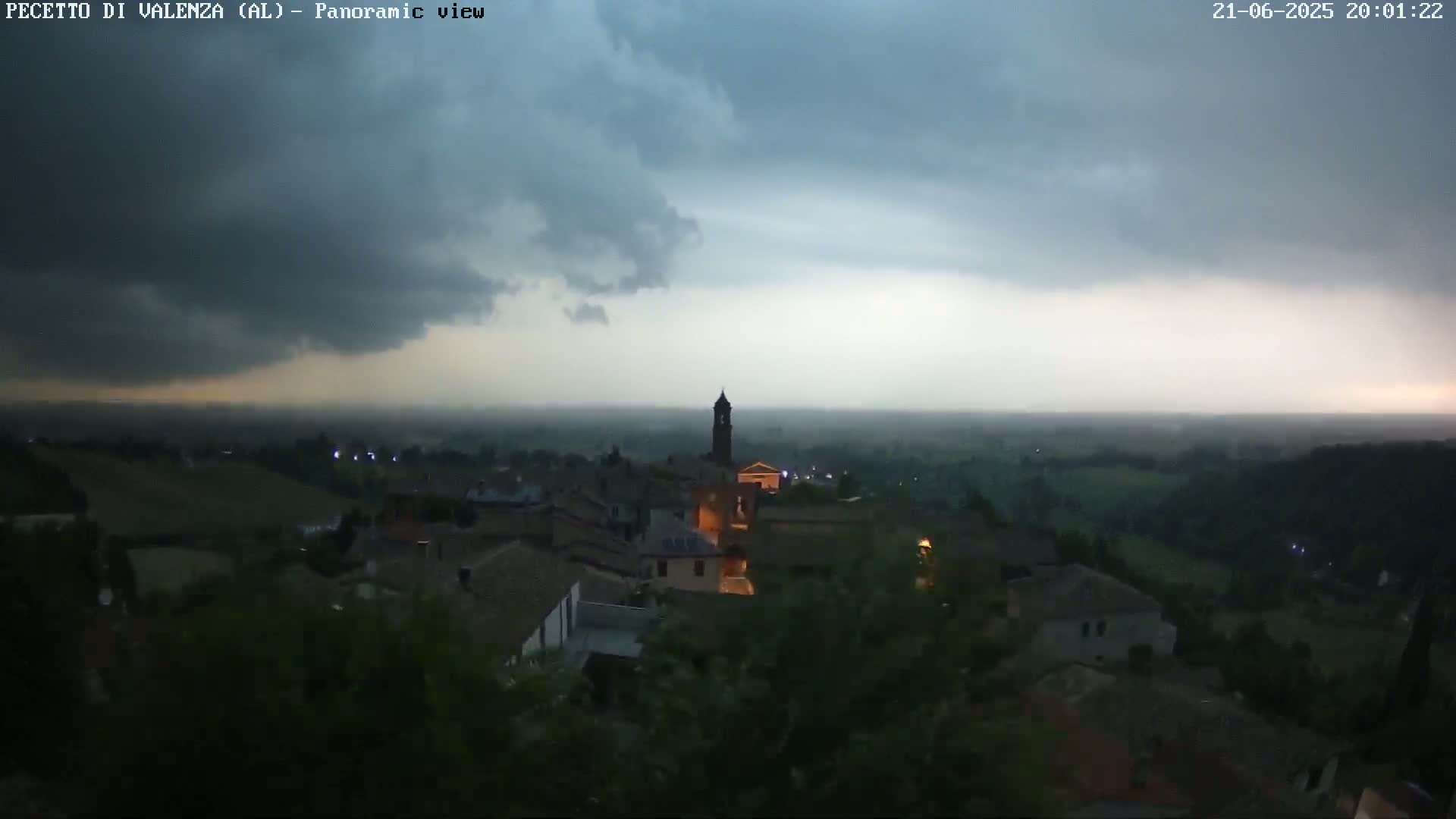 A small town with a bell tower is seen under a large, dark storm cloud at dusk.