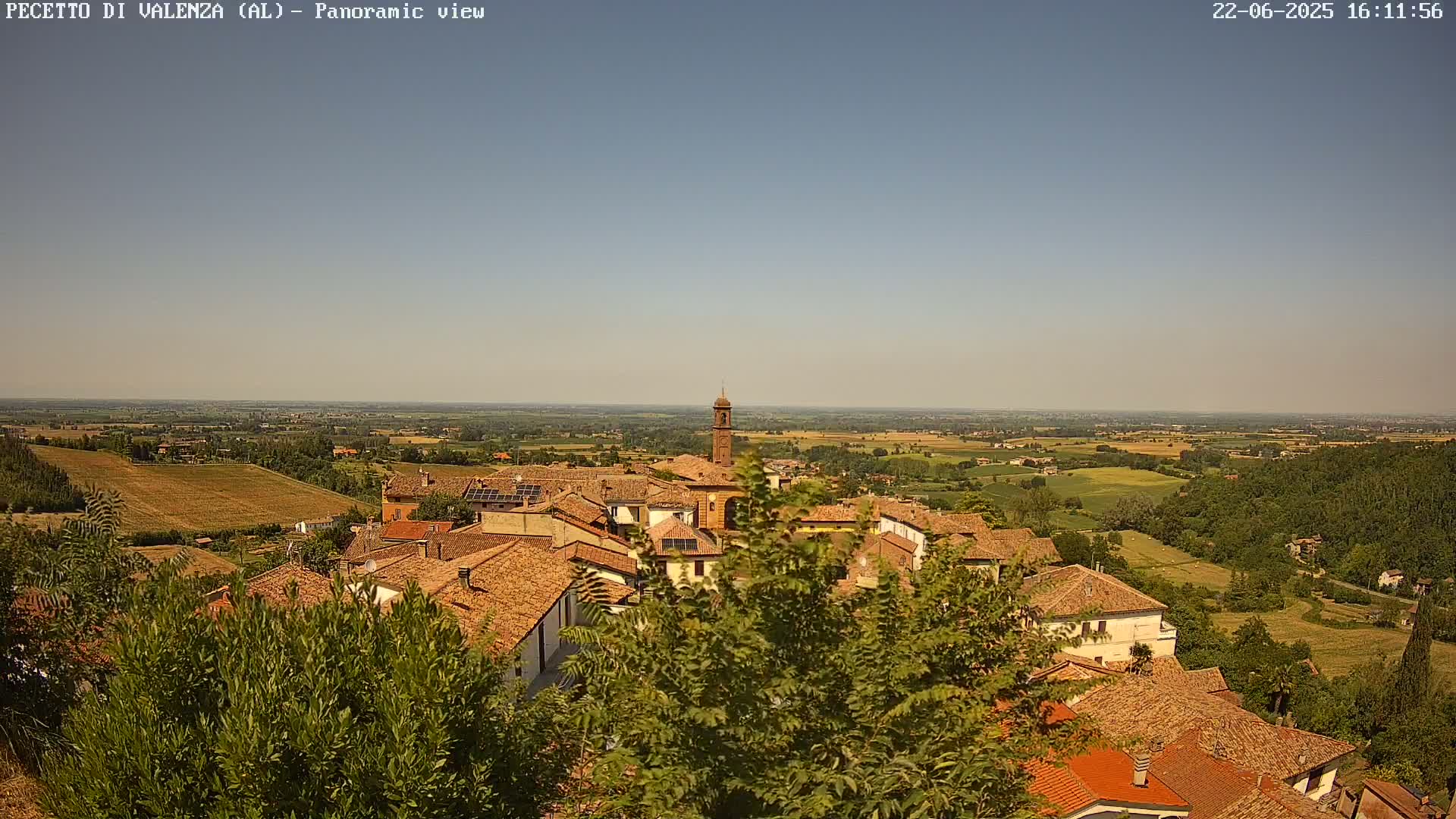 A panoramic view shows a small town nestled in a valley on a sunny day, with rolling hills and farmland stretching out to the horizon.