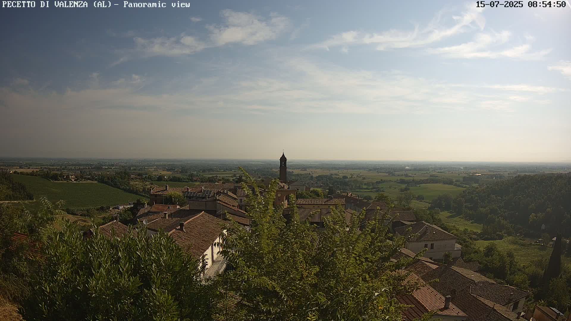 A panoramic view of a town nestled in a hilly landscape under a partly cloudy sky.