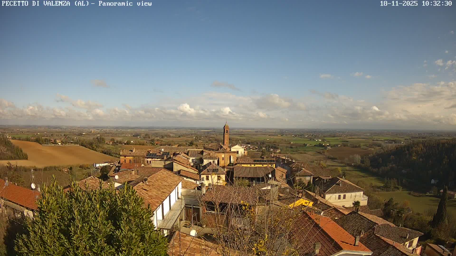 The image captures a panoramic view of a village with terracotta roofs and trees, largely obscured by thick, heavy fog.