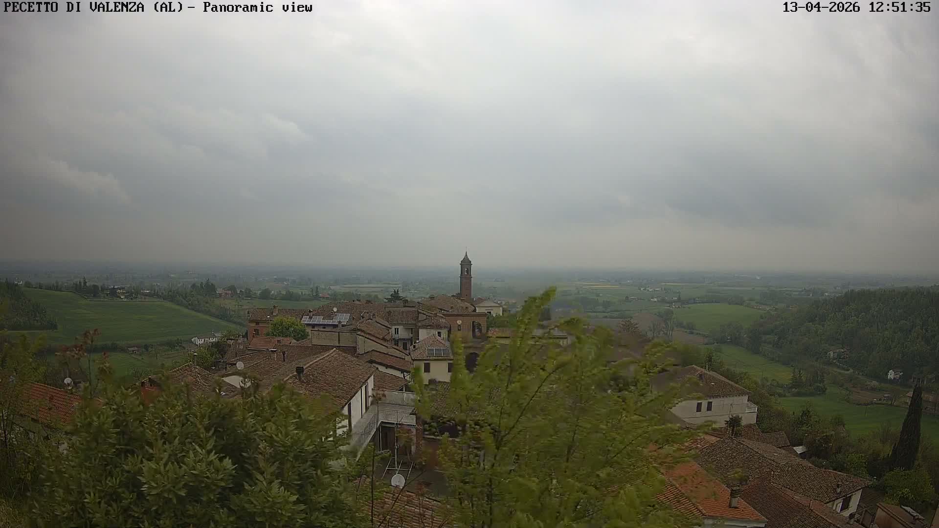 A panoramic view of a town with numerous buildings and red-tiled roofs is enveloped in thick fog, obscuring the distant landscape.