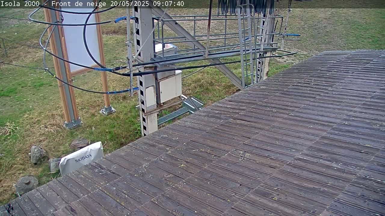 A dark-wood deck extends from a metal ski lift structure situated in a grassy area on an overcast day.