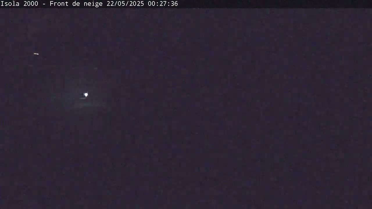 A dark, nighttime scene shows a bright light in the distance under a mostly clear sky.