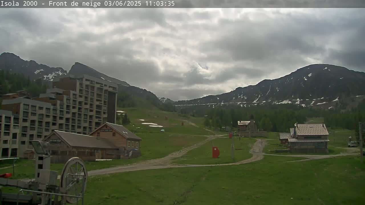 A mountain resort town under a cloudy sky, featuring a large hotel, several smaller buildings, and a grassy valley.