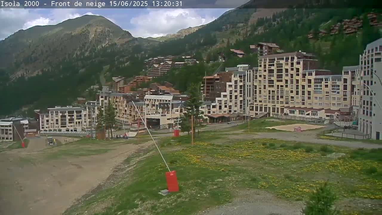 A mountainside village with several multi-story buildings is visible under partly cloudy skies.