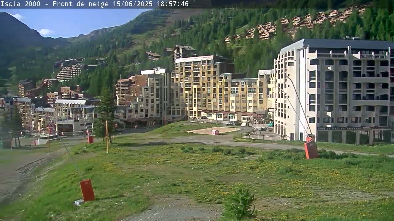 A sunny view of a cluster of multi-story buildings nestled in a mountainous, green valley.