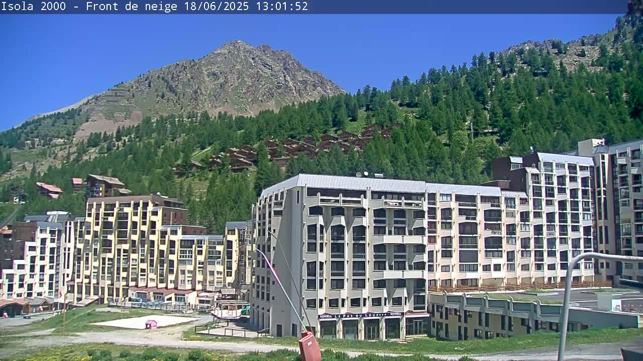 A mountainside residential area with numerous multi-story buildings is visible under a clear, sunny sky.