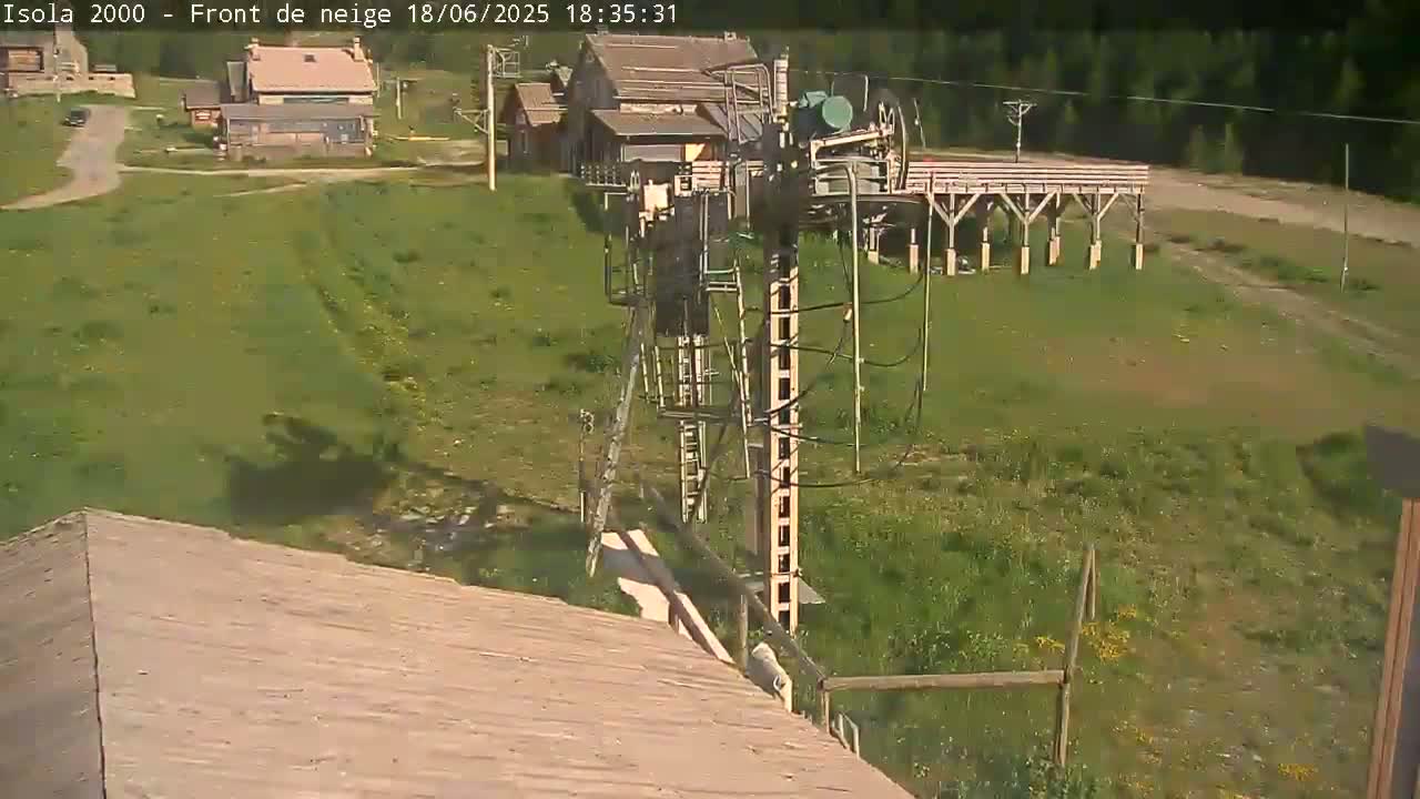 A ski lift mechanism is situated on a grassy hill, with buildings visible in the background on a sunny day.