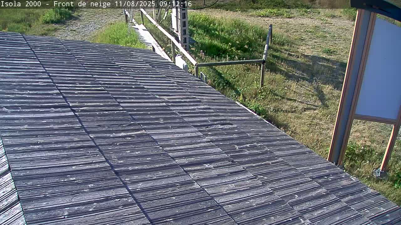 A dark gray sloped wooden surface extends from the foreground into the midground, where it meets grassy terrain under a sunny sky.