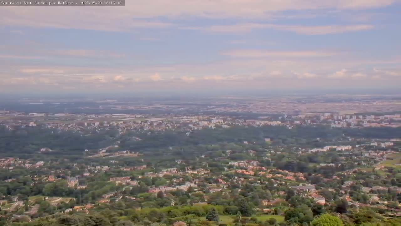 A sprawling suburban landscape under a partly cloudy sky stretches to a distant city on the horizon.