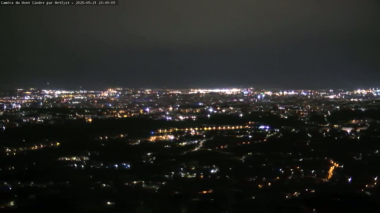 A nighttime, high-angle view of a city's lights spread across a dark landscape under a mostly clear sky.