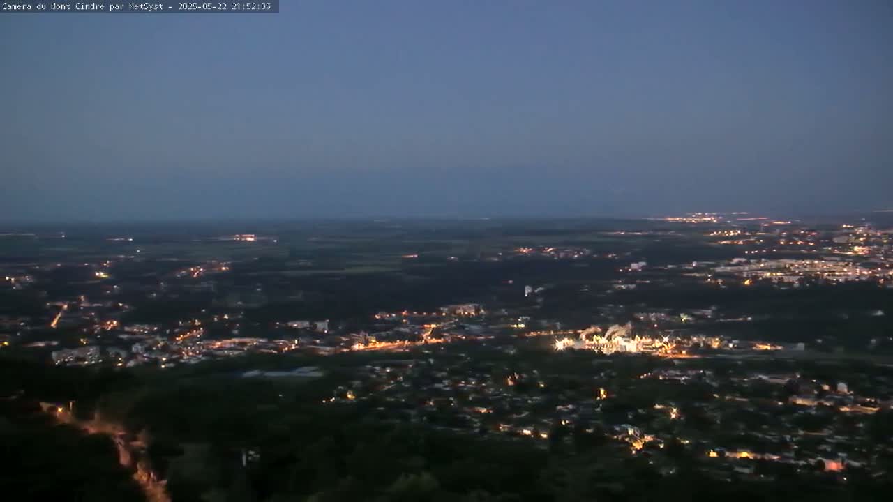 A nighttime, high-angle view shows a sprawling city illuminated by scattered lights under a clear, dusky sky.