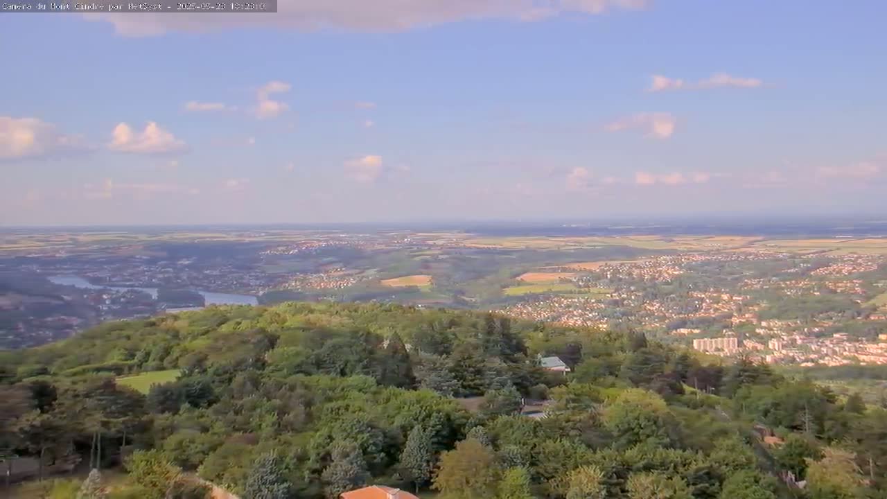 A sprawling view of a verdant landscape, featuring a river winding through a valley populated by towns and villages, under a partly cloudy sky.