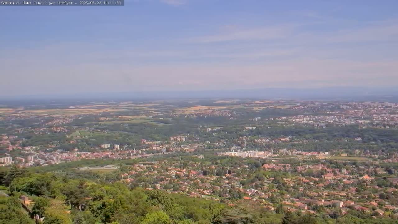 A sprawling suburban landscape under a mostly clear sky stretches to the horizon, showing a mix of houses, trees, and open fields.