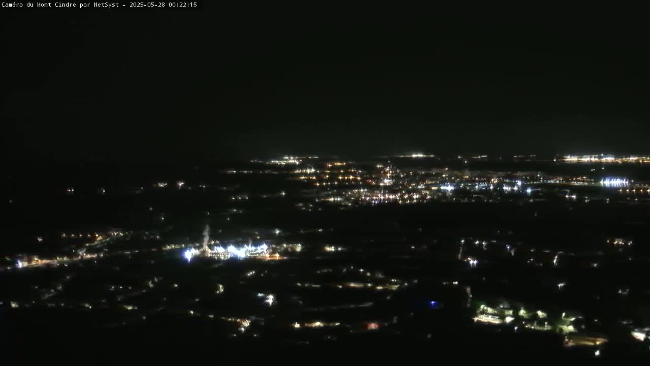 A nighttime, high-angle view shows a sprawling city illuminated by scattered lights, extending to the horizon under a clear, dark sky.