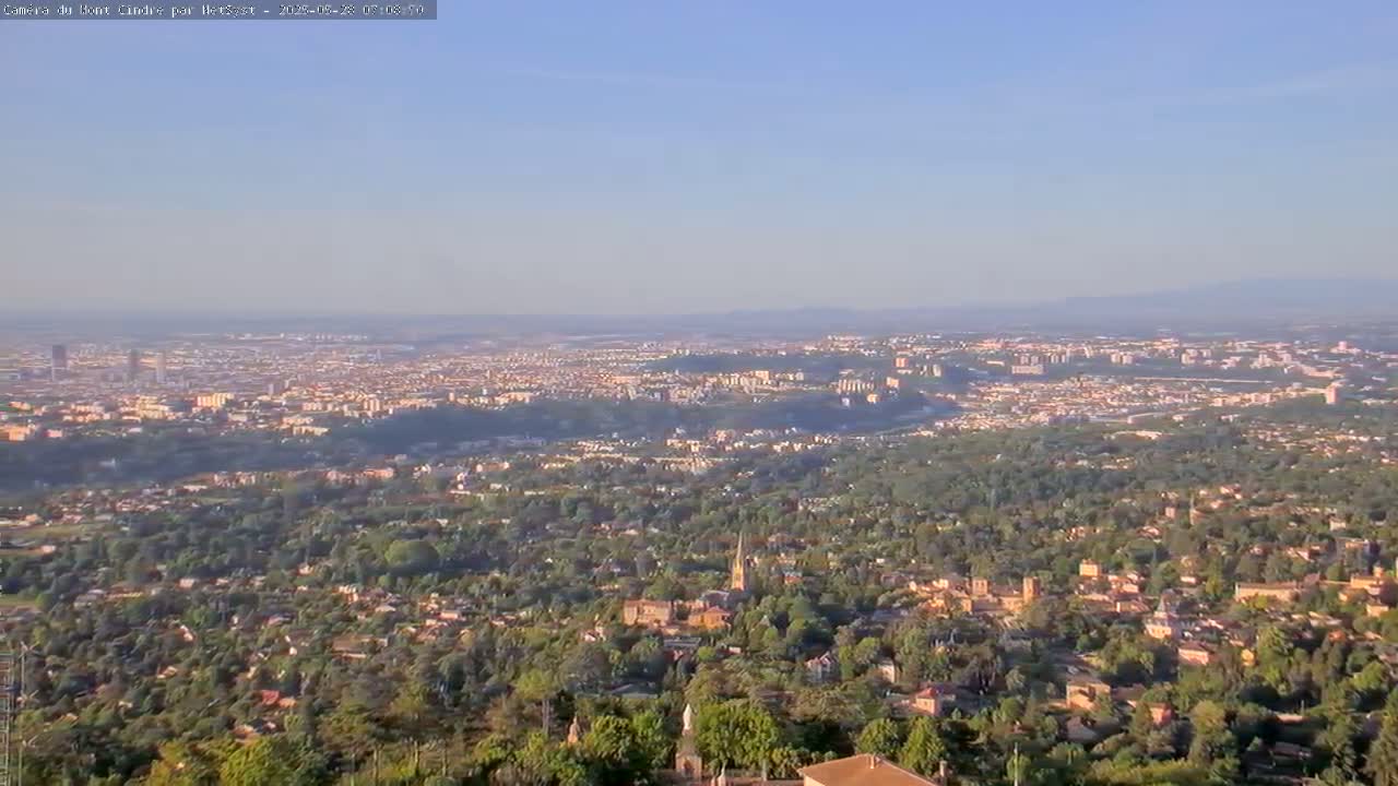 A sprawling city and its surrounding suburbs are visible from a high vantage point on a clear, sunny day.