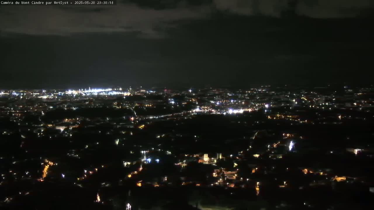 A nighttime, high-angle view shows a sprawling city illuminated by scattered lights under a mostly cloudy sky.