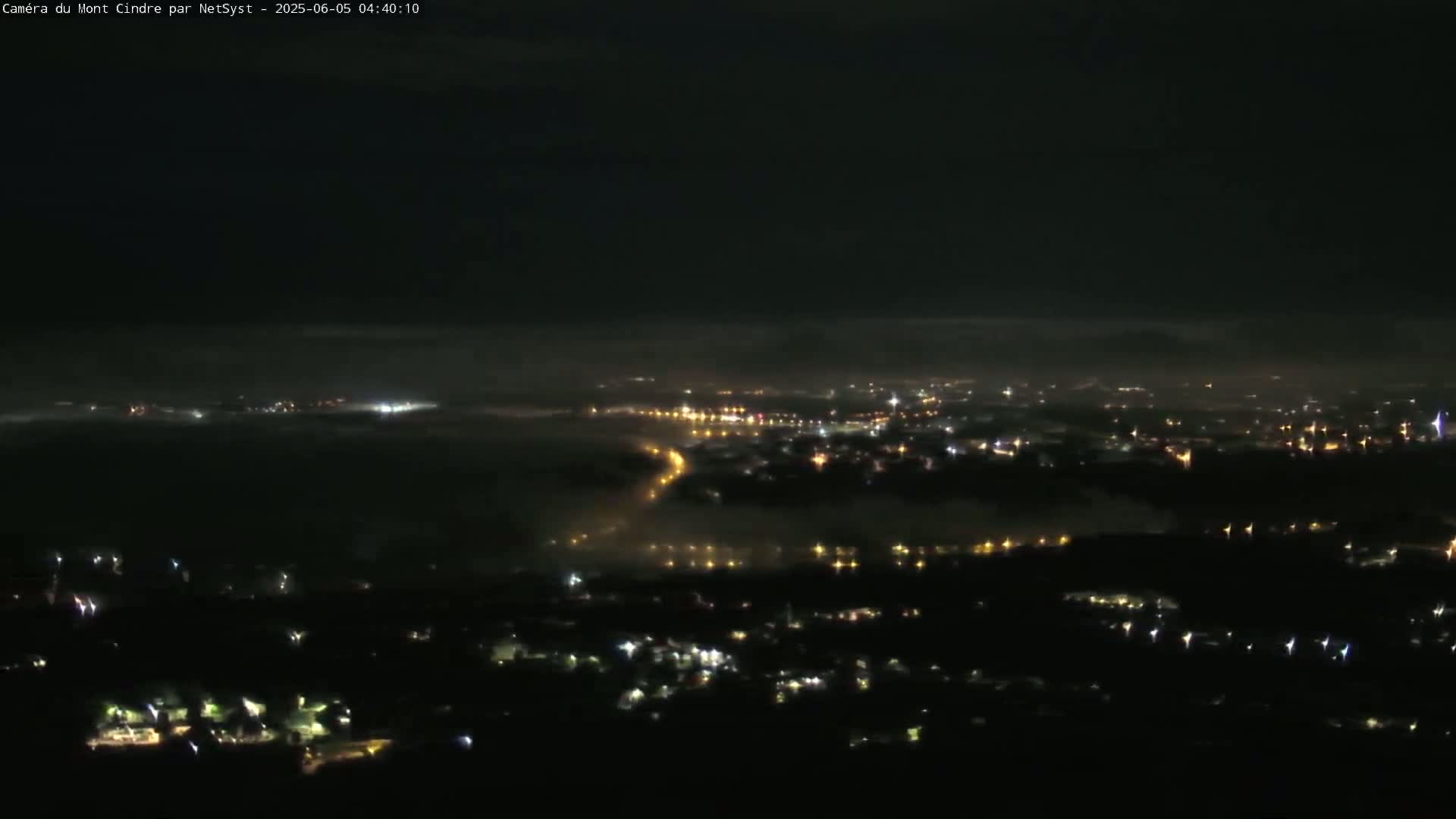 A nighttime, high-angle view shows a city shrouded in fog or low clouds, with scattered lights visible through the haze.