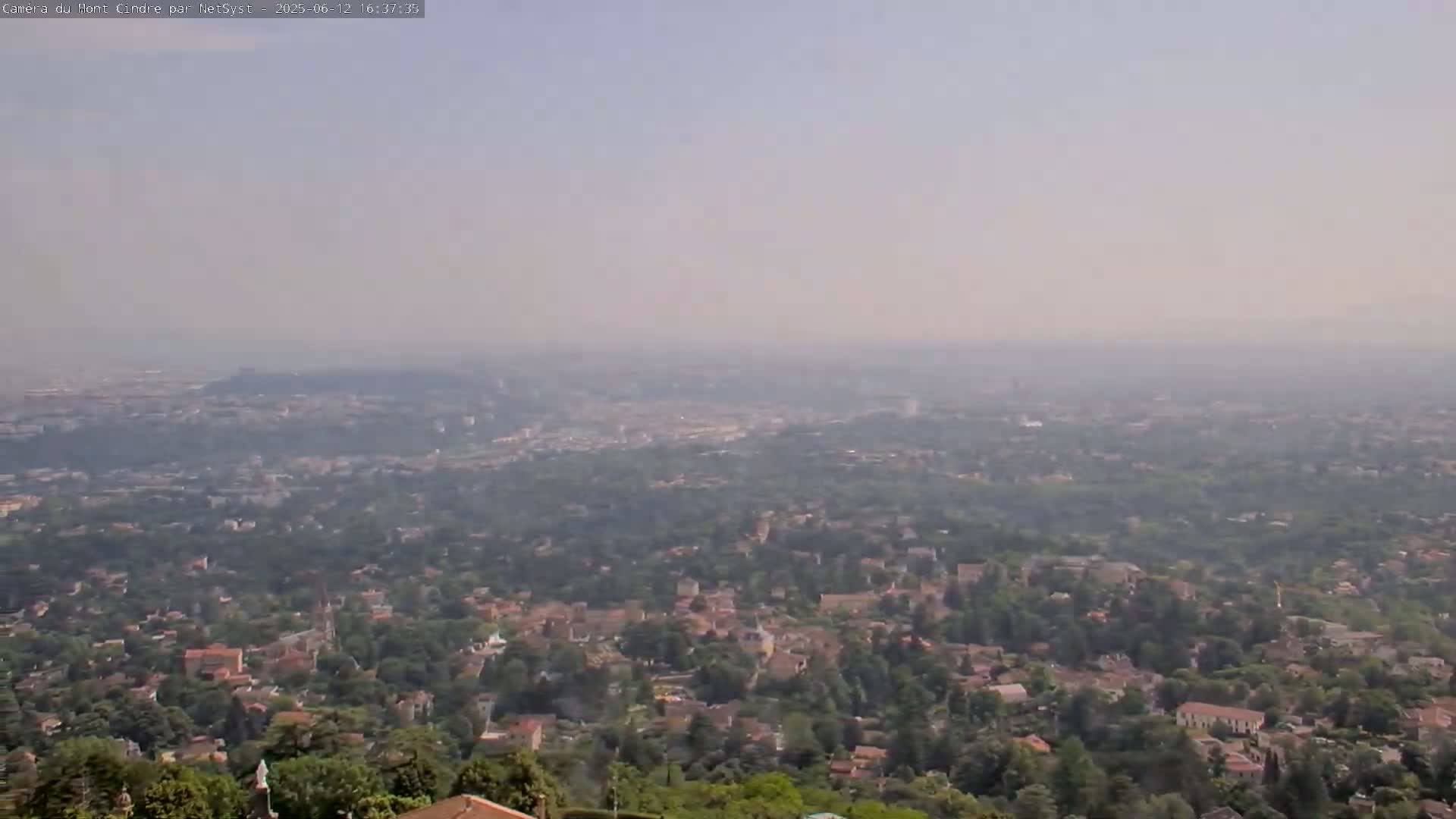 A hazy, distant view of a sprawling town or city nestled among green trees and hills.