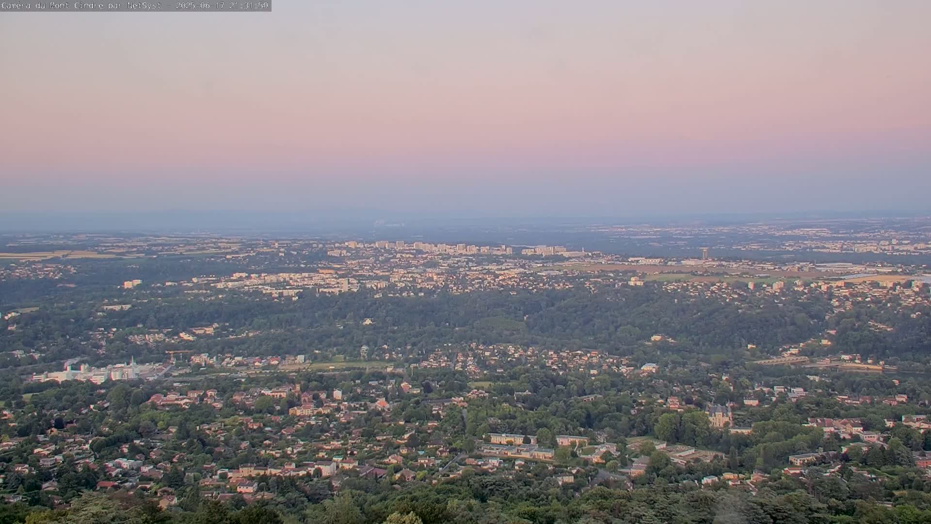 A sprawling suburban landscape under a pale pink sunset sky stretches to the horizon.