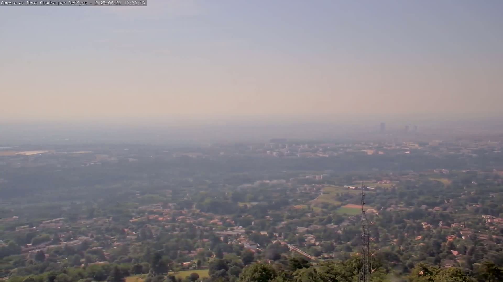 A hazy, long-range view shows a sprawling suburban area extending to a distant city skyline under a light-colored sky.