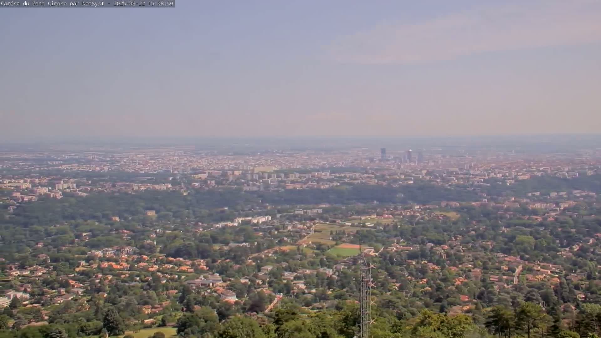A hazy view shows a sprawling city in the distance, with suburban neighborhoods and green spaces in the foreground.