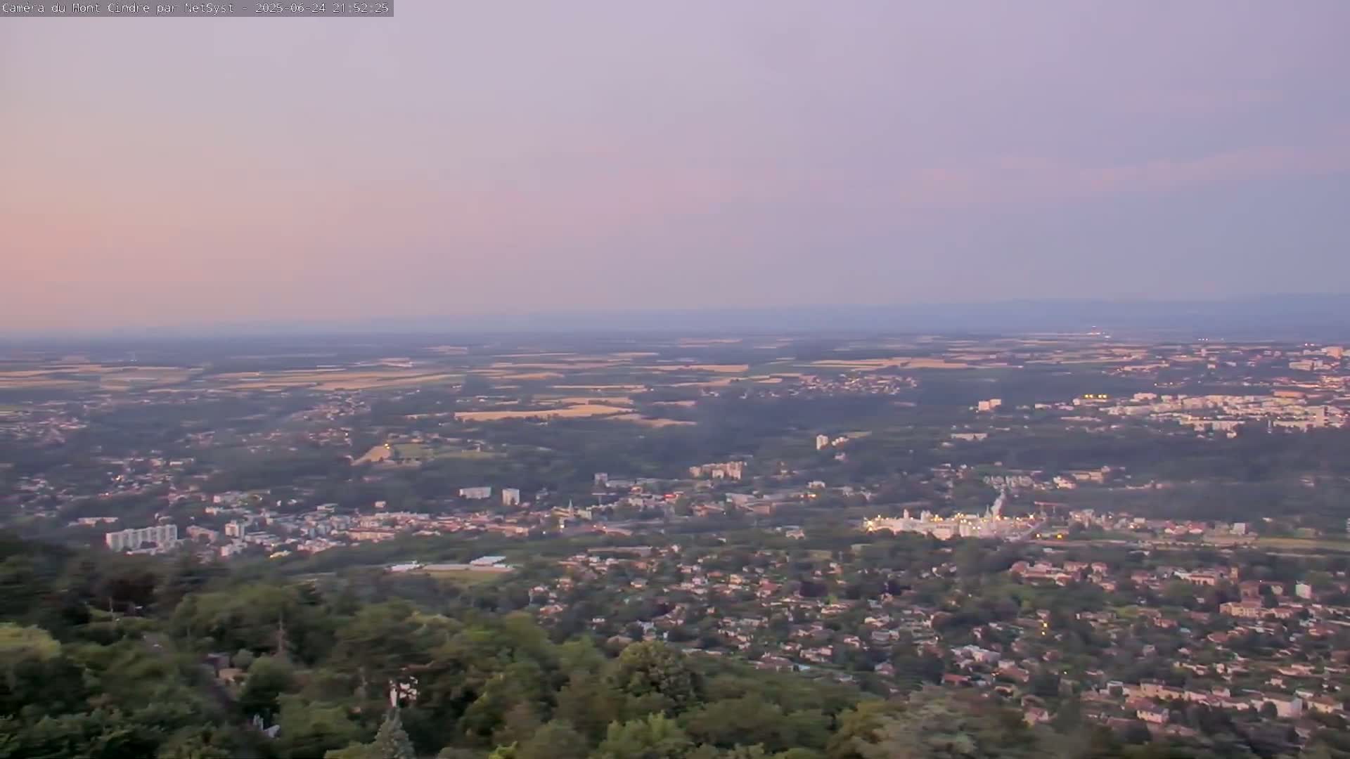 A sprawling town and surrounding countryside are visible from a high vantage point under a pale, dusky sky.