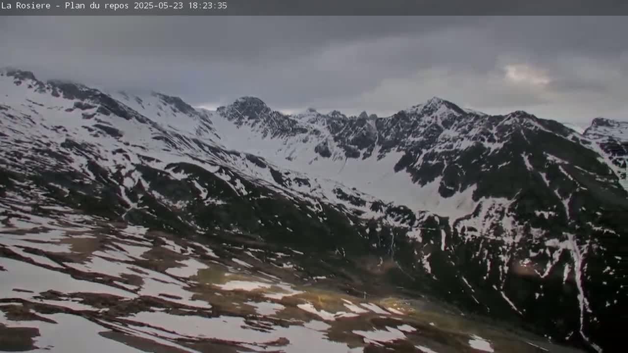 A snow-dusted mountain range stretches under a cloudy sky.