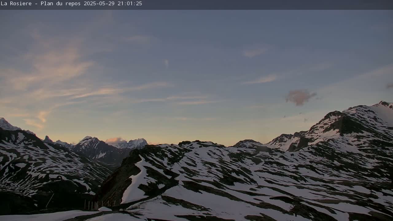 A snow-dusted mountain range is visible under a twilight sky with thin clouds.